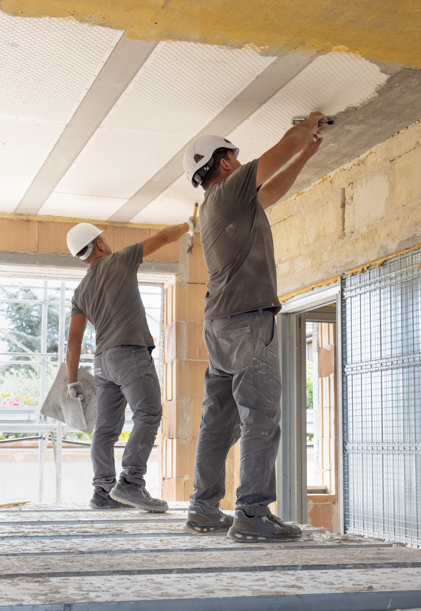 Craftsmen in grey clothes working inside a room standing on scaffoldings during construction